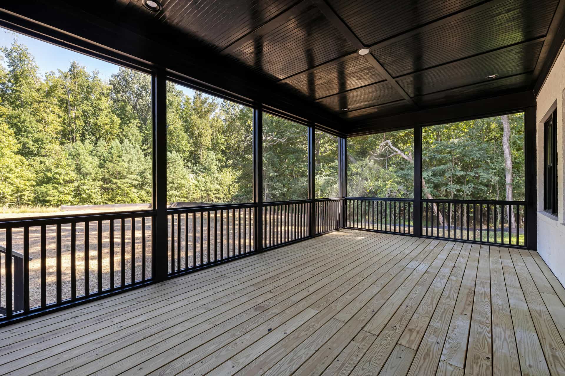 Screened porch with a dark stained ceiling, black railings and a wooded view